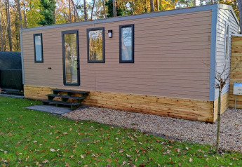 Modern Luxe Homes-lodge bij Bospark De Brenkberg in Nederland, omgeven door groen gras en bomen.