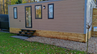 Lodge moderno Luxe Homes al Bospark De Brenkberg, Paesi Bassi, circondato da prato verde e alberi.