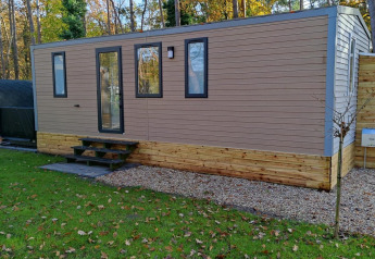 Lodge moderno Luxe Homes al Bospark De Brenkberg, Paesi Bassi, circondato da prato verde e alberi.