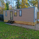 Et moderne Luxe Homes-lodge ved Bospark De Brenkberg i Holland, omgivet af grøn plæne og træer.