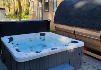 Vasca idromassaggio e sauna a botte all’aperto davanti a un lodge in Luxe Homes, Bospark De Brenkberg, Paesi Bassi.