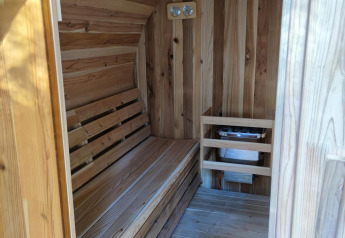 Interior de una sauna de madera en Luxe Homes, Bospark De Brenkberg, Países Bajos, con banco y calentador.