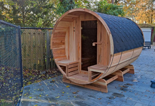 Sauna de barril de madera al aire libre en Luxe Homes, Bospark De Brenkberg, Países Bajos, rodeada de árboles.
