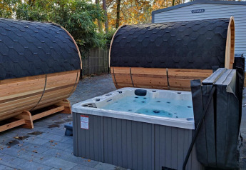 Area spa all'aperto con due saune a botte e una vasca idromassaggio a Luxe Homes, Bospark De Brenkberg, Paesi Bassi.