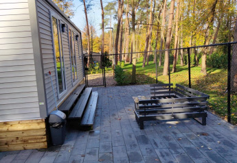 Moderne lodge met buitenterras en bank bij Bospark De Brenkberg, Nederland, omgeven door hoge bomen.