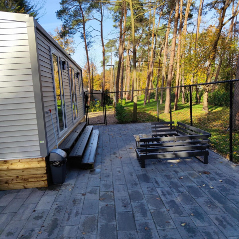 Lodge moderne avec terrasse et banc extérieur au Bospark De Brenkberg aux Pays-Bas, entouré d’arbres.