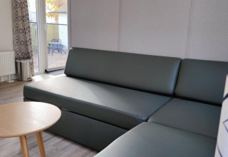 Modernes Wohnzimmer mit grauem Sofa, rundem Holztisch und großen Fenstern in einer Lodge bei Bospark De Brenkberg.