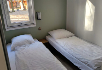 Deux lits simples avec draps blancs dans une chambre lumineuse chez Luxe Homes, Bospark De Brenkberg, Pays-Bas.