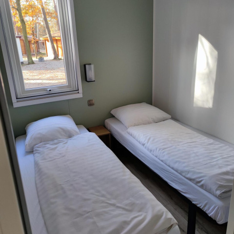 Dos camas individuales con sábanas blancas en una habitación luminosa en Luxe Homes, Bospark De Brenkberg, Países Bajos.