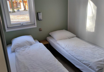 Deux lits simples avec draps blancs dans une chambre lumineuse chez Luxe Homes, Bospark De Brenkberg, Pays-Bas.