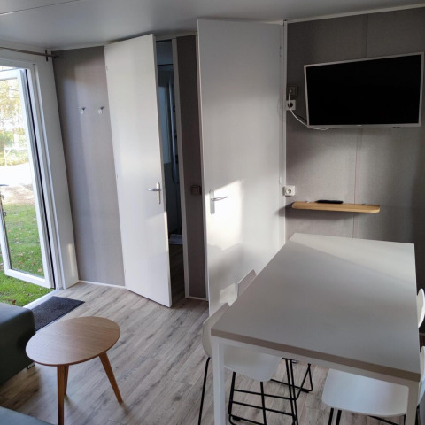 Vista interior de un moderno lodge en Luxe Homes, Bospark De Brenkberg, con mesa, sillas y televisor en la pared.