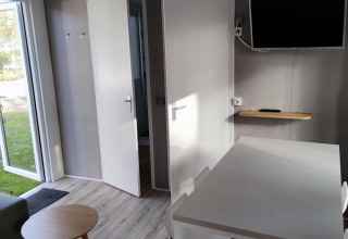 Vista interior de un moderno lodge en Luxe Homes, Bospark De Brenkberg, con mesa, sillas y televisor en la pared.