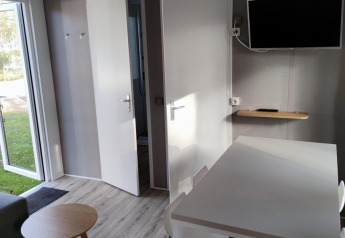 Vista interna di un moderno lodge a Luxe Homes, Bospark De Brenkberg, con tavolo, sedie e TV a parete.