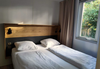 Moderne slaapkamer met tweepersoonsbed, houten hoofdbord en raam bij Luxe Homes op Bospark De Brenkberg.