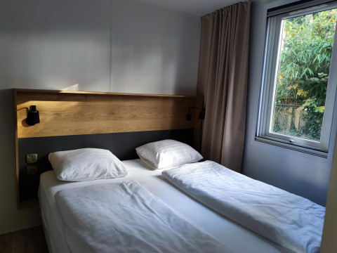 Dormitorio moderno con cama doble, cabecero de madera y ventana en Luxe Homes de Bospark De Brenkberg, Países Bajos.