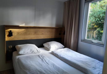 Dormitorio moderno con cama doble, cabecero de madera y ventana en Luxe Homes de Bospark De Brenkberg, Países Bajos.