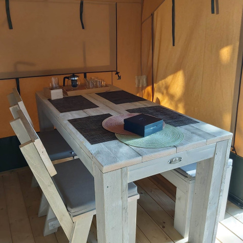 Interior de tienda safari glamping con mesa y bancos de madera y manteles en Camping Batenstein, Países Bajos.