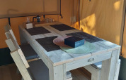 Interior of a glamping safari tent with wooden table, benches, and placemats at Camping Batenstein, Netherlands.