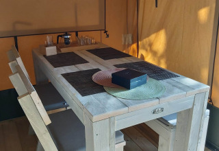 Interior de tienda safari glamping con mesa y bancos de madera y manteles en Camping Batenstein, Países Bajos.