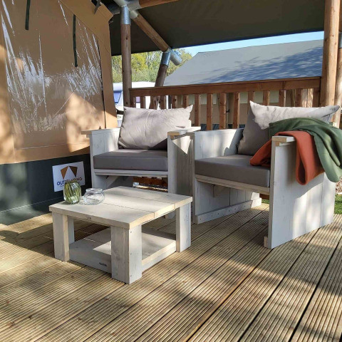 Zona de estar exterior con muebles de madera clara en una tienda glamping en Camping Batenstein, Países Bajos.
