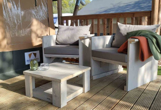 Zona de estar exterior con muebles de madera clara en una tienda glamping en Camping Batenstein, Países Bajos.