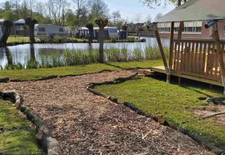 Zicht op een glamping safaritent bij Camping Batenstein, Nederland, met houtsnipperpad langs vijver.