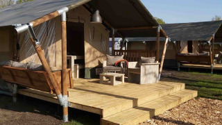 Tienda safari de glamping de lujo con terraza de madera, columpio y cómodos muebles de exterior al sol.