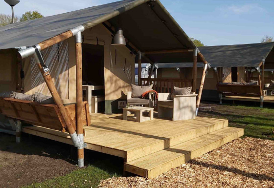 Tienda safari de glamping de lujo con terraza de madera, columpio y cómodos muebles de exterior al sol.