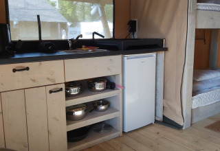 Interior de una tienda safari glamping con cocina pequeña, frigorífico y literas en Camping Batenstein, Países Bajos.