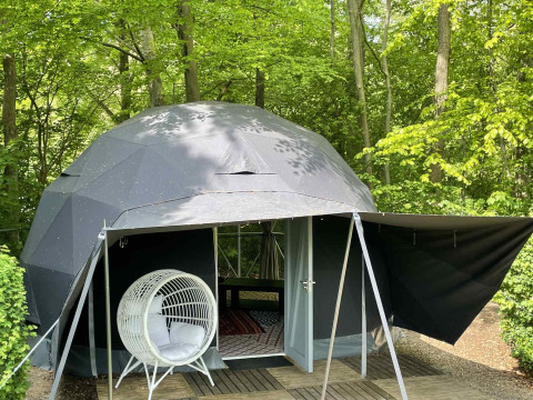 Tienda de cúpula geodésica rodeada de bosque en Buytenplaets Abelen, Flevoland, Países Bajos, con silla colgante.