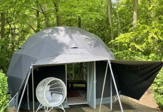 Geodetische koepeltent in de natuur van Buytenplaets Abelen, Flevoland, Nederland, met een witte hangstoel ervoor.