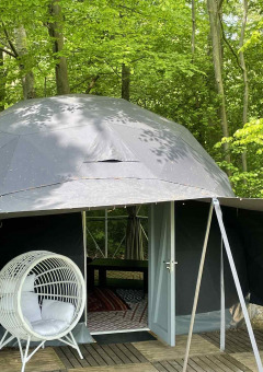 Tienda de cúpula geodésica rodeada de bosque en Buytenplaets Abelen, Flevoland, Países Bajos, con silla colgante.