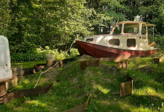 A small boat sits on the grass in a forest clearing at Buytenplaets Suydersee holiday park, Flevoland.