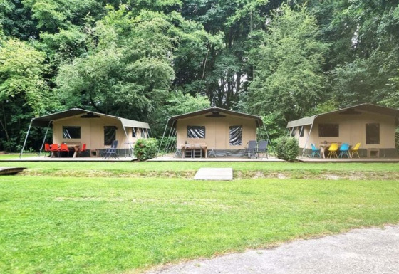 Tres tiendas safari con sillas de colores al aire libre en Buytenplaets Suydersee, Países Bajos, junto a un bosque.