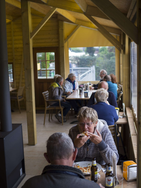 Personas disfrutan comida y bebida en mesas de madera en Camping De Grienduil, parque vacacional en Utrecht, Países Bajos.
