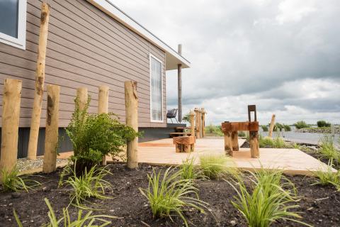 Waterlodge type 1 at Vakantiepark Bergumermeer in the Netherlands with wooden patio and garden chairs.