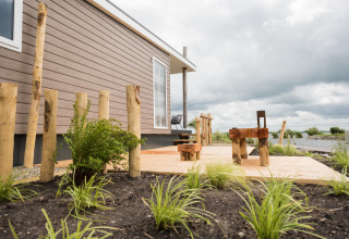 Blick auf Waterlodge Typ 1 im Vakantiepark Bergumermeer mit Holzterrasse und rustikalen Sitzmöbeln.