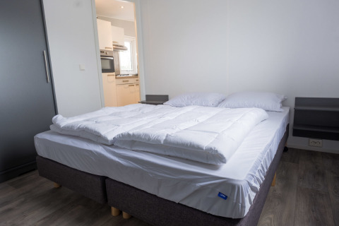 Soveværelse med dobbeltseng og hvide sengeklæder i Waterlodge type 1 på Vakantiepark Bergumermeer, Holland.