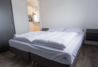 Dormitorio con cama doble y ropa de cama blanca en Waterlodge tipo 1 en Vakantiepark Bergumermeer, Países Bajos.