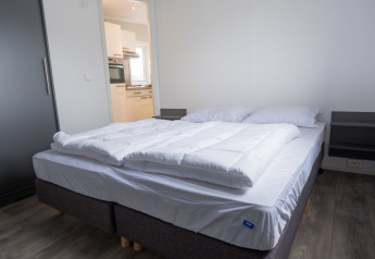 Dormitorio con cama doble y ropa de cama blanca en Waterlodge tipo 1 en Vakantiepark Bergumermeer, Países Bajos.