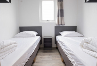 Værelse med to enkeltsenge, et lille natbord og moderne indretning i Waterlodge type 1, Vakantiepark Bergumermeer.