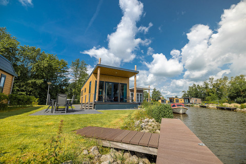 Moderna waterlodge junto al lago con terraza, muebles de jardín y barco en Vakantiepark Bergumermeer, Países Bajos.