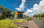 Moderne waterlodge ved søen med terrasse, havemøbler og båd ved Vakantiepark Bergumermeer, Holland.