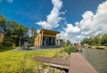 Moderne waterlodge ved søen med terrasse, havemøbler og båd ved Vakantiepark Bergumermeer, Holland.