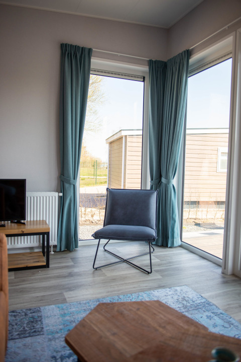 Modern chair and blue curtains by large windows in Waterlodge type 1 at Vakantiepark Bergumermeer, Netherlands.