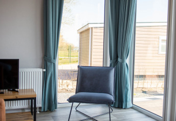Fauteuil moderne et rideaux bleus près de grandes fenêtres à la Waterlodge type 1, Vakantiepark Bergumermeer, Pays-Bas.