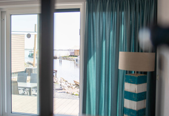 Udsigt fra Waterlodge type 1 på Vakantiepark Bergumermeer med lys stue, blå gardiner og terrasse.