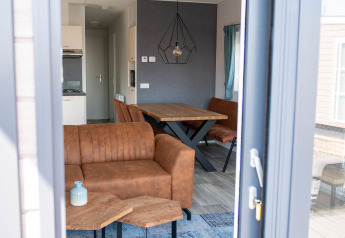 Udsigt ind i en moderne lodge med brune sofaer og spisebord på Waterlodge type 1, Vakantiepark Bergumermeer.