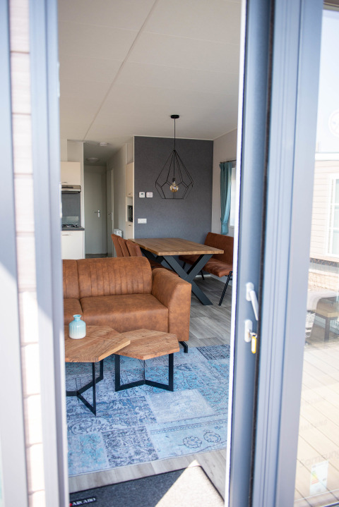 Blick in eine moderne Lodge mit braunen Sofas und Esstisch im Waterlodge Typ 1, Vakantiepark Bergumermeer.