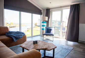 Lys stue i Waterlodge type 2 med store vinduer, udsigt til vandet og moderne møblering.